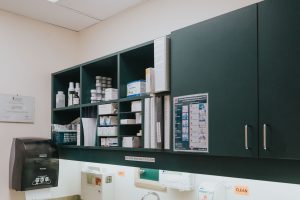 A green cupboard full of medical supplies and boxes.