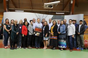 A group of approximately 15 people stand posing for a picture in front of a banner at Siksika First Nation,