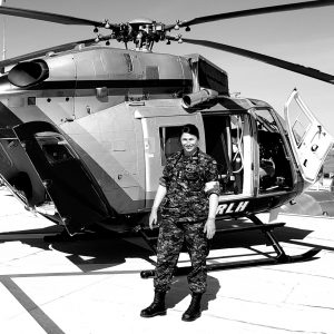 A woman stands in front of a helicopter in a military uniform. 