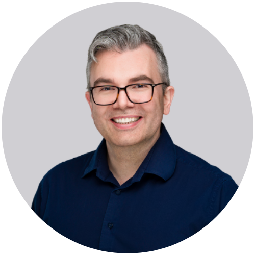 A man with glasses smiling for a professional headshot