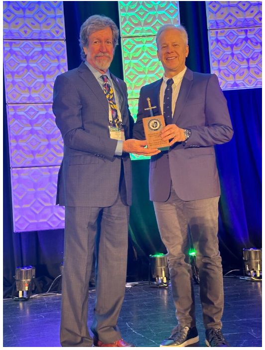 Two men standing on a stage holding a plaque